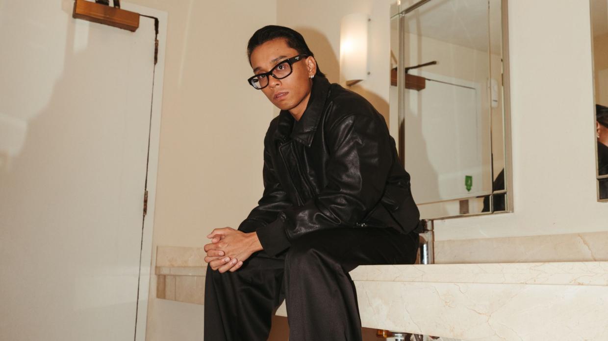 Photo of a man wearing black sitting near a mirror .