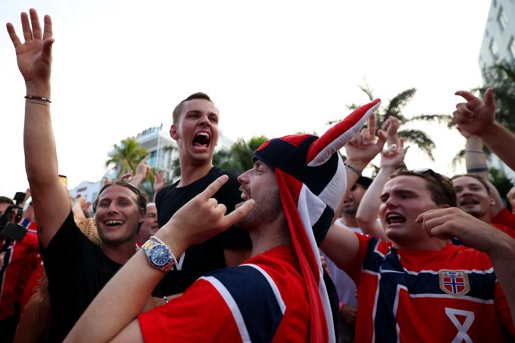 Photo of Norway fans in Miami for the World Cup. The fan in the front stands in profile wearing a Viking hat and putting up devil horns