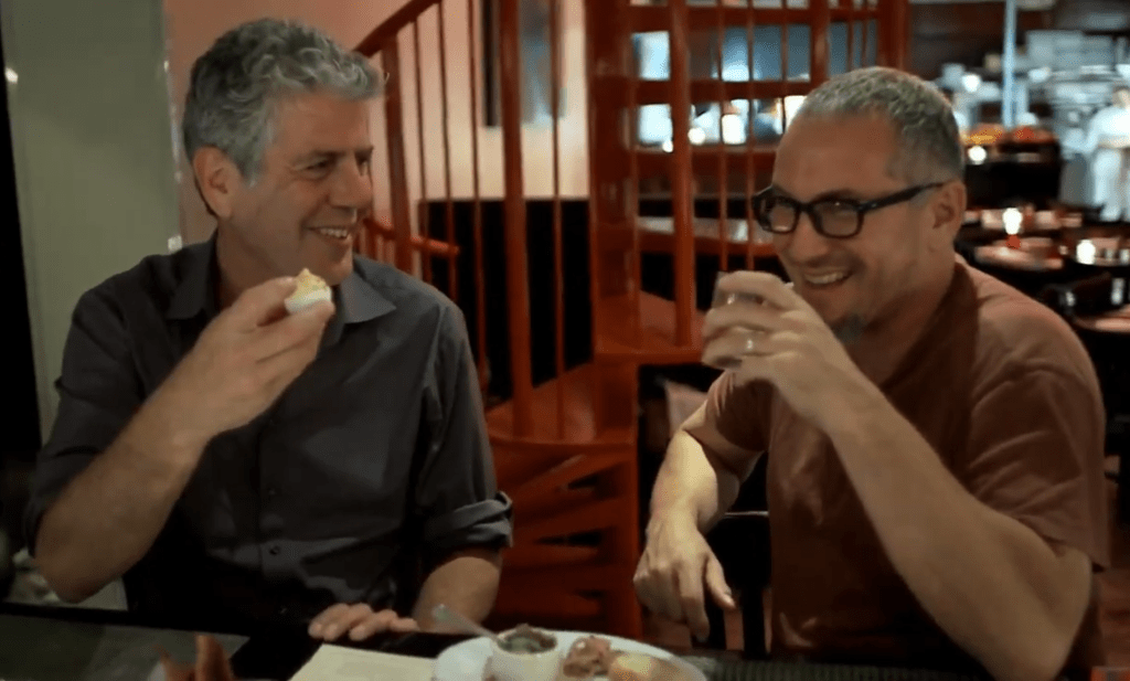 two men laughing at a table holding drinks
