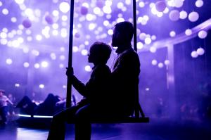 photo of a man and child in shadow sitting on a swing inside an art museum with purple lighting all around them