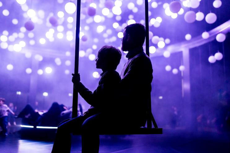 photo of a man and child in shadow sitting on a swing inside an art museum with purple lighting all around them