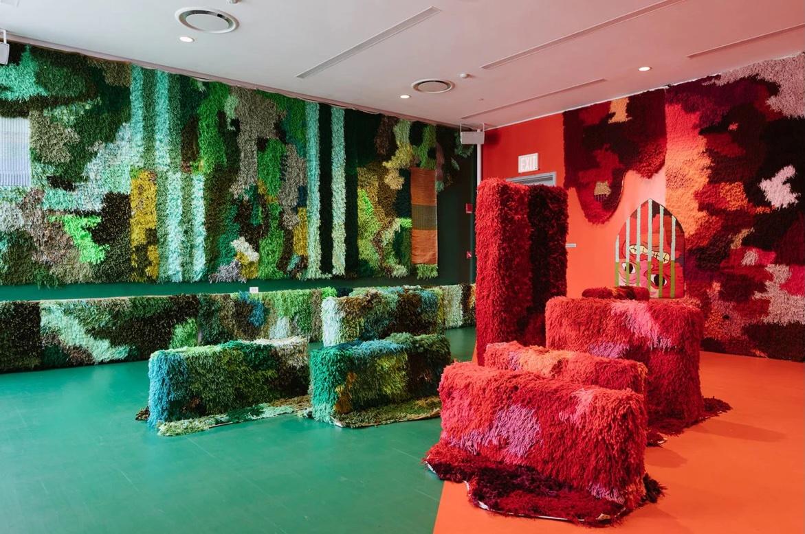 photo of an art installation featuring a half-green, half-red-orange room with floors and structures overlayed with a fuzzy fabric in those corresponding colors