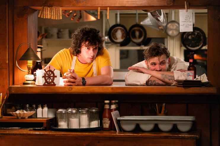 Film still from the movie "Tony depicting two men leaning on the counter of a restaurant kitchen