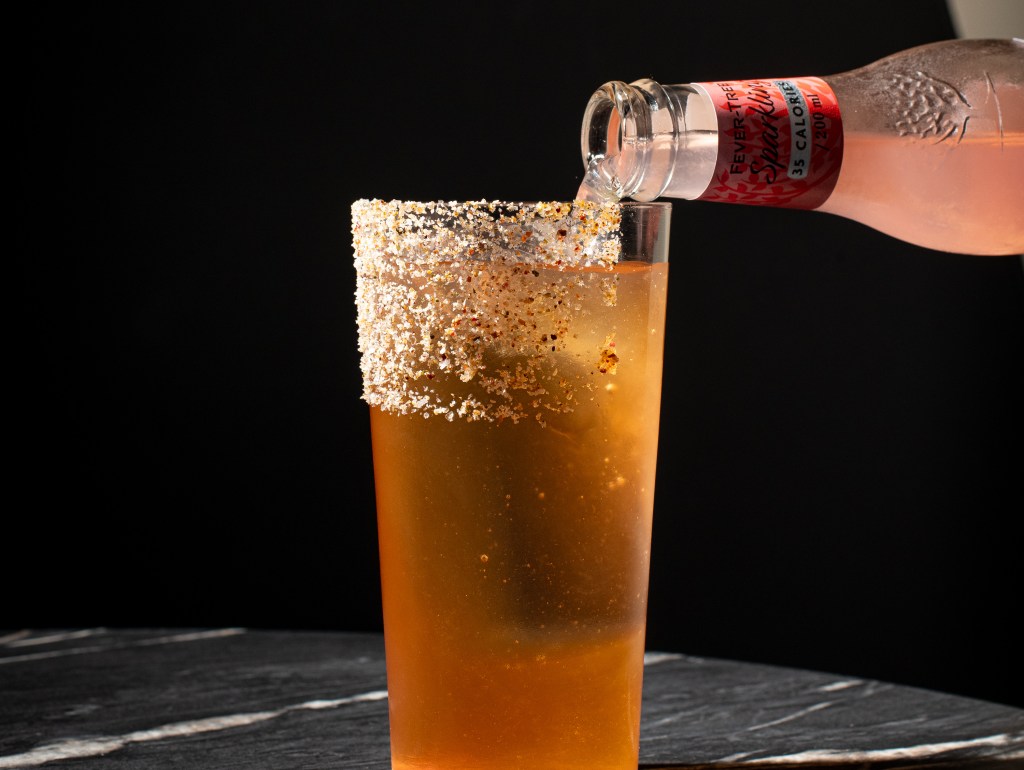 a tall brown cocktail with a sugar rim and a pink bottle next to it