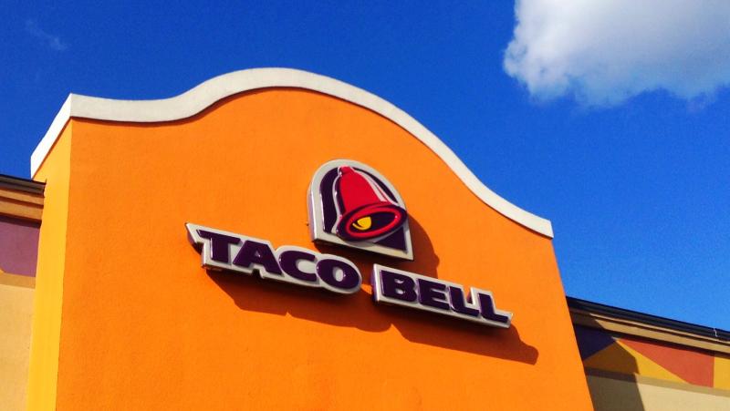 orange exterior of a Taco Bell, featuring Taco Bell lettering in purple against a blue sky