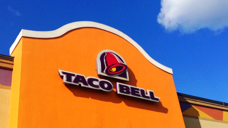 orange exterior of a Taco Bell, featuring Taco Bell lettering in purple against a blue sky