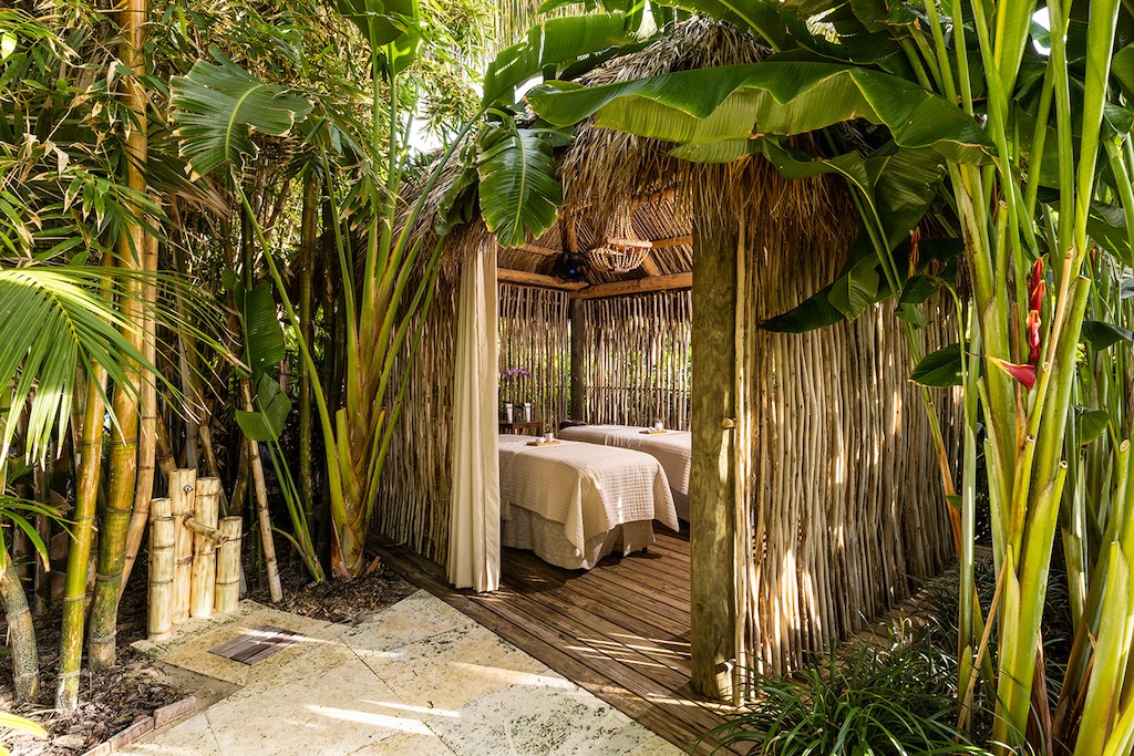 photo of two massage beds inside a thatched outdoor structure surrounded by palms