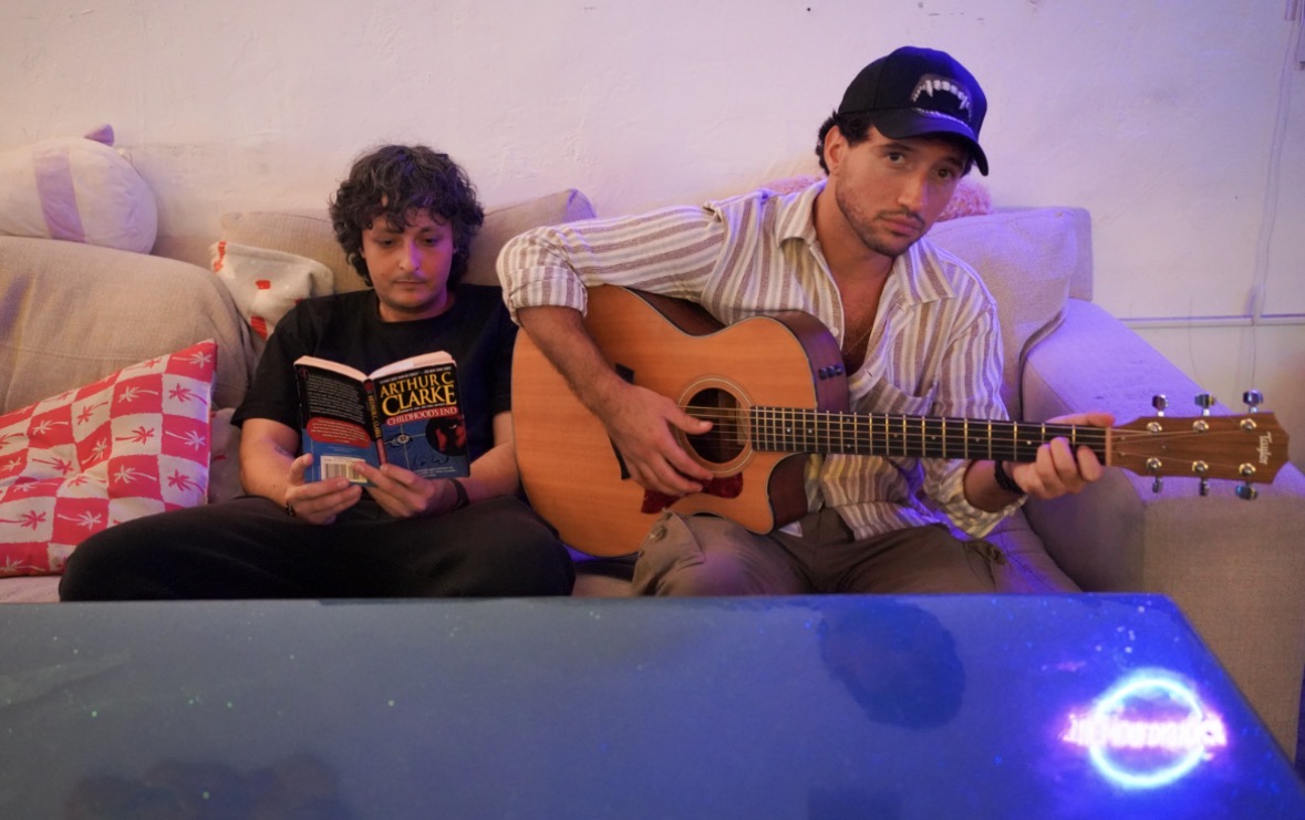 Two people sitting on a couch in Miami, one is reading a book and the other playing guitar.