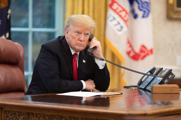 a suited man sits in an office holding a phone to his ear