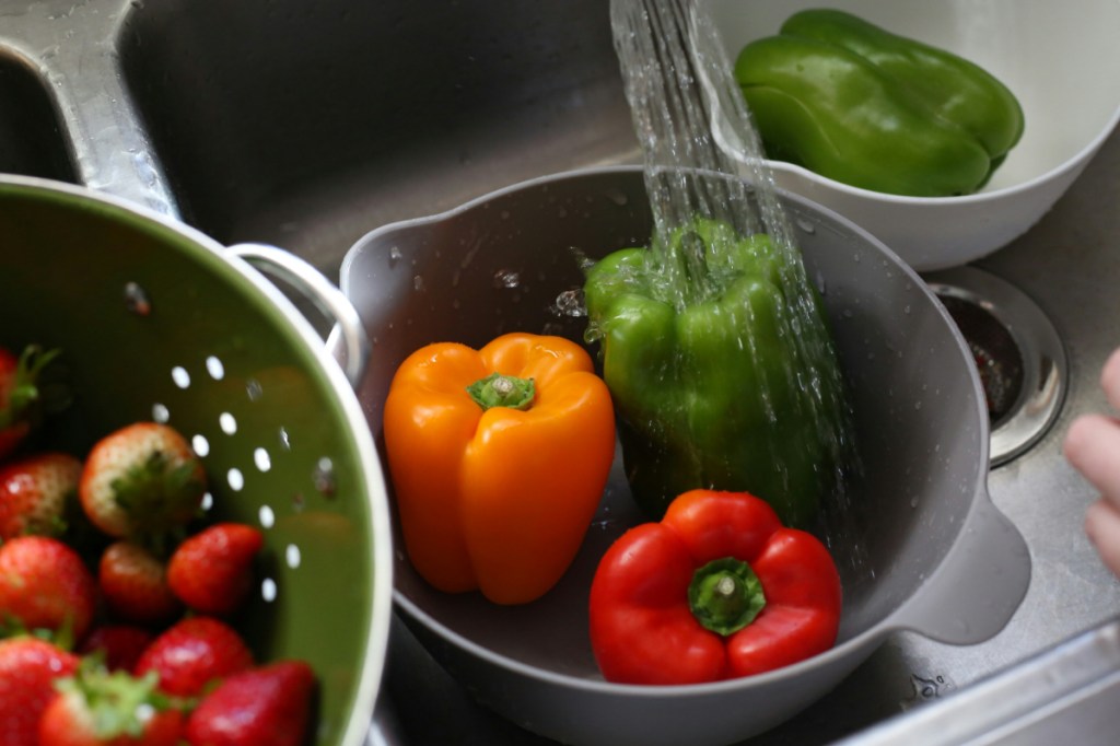 A photo of peppers and strawberries being washed in a sink.