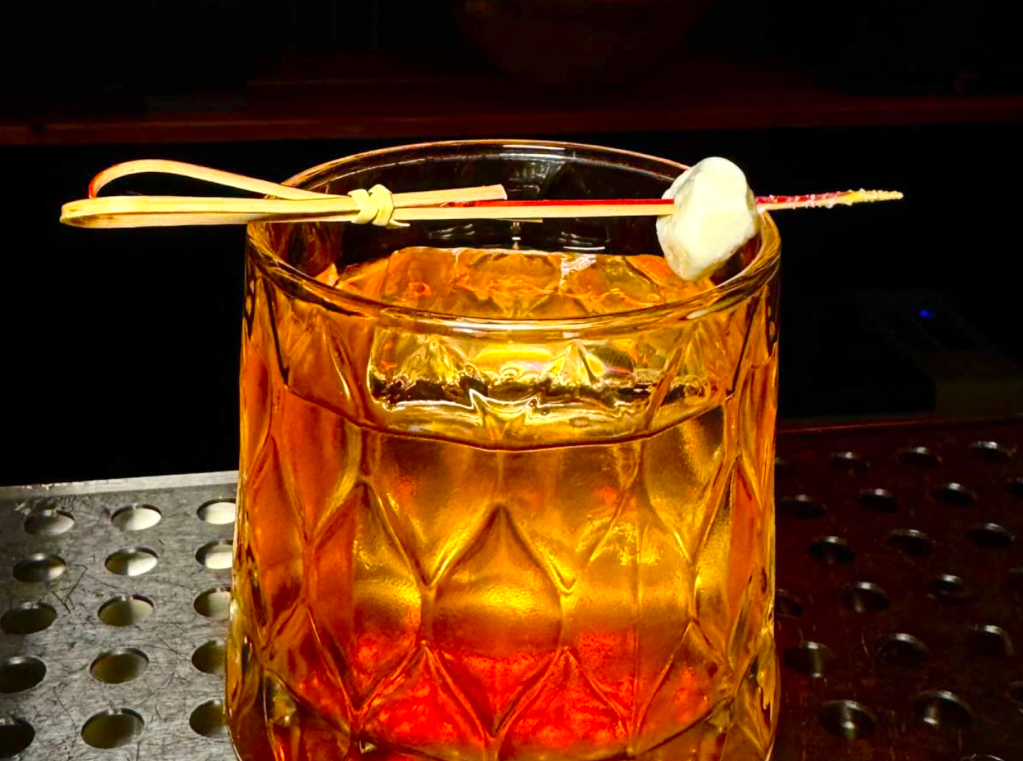 an orange cocktail in a short cocktail glass with a bamboo garnish pick