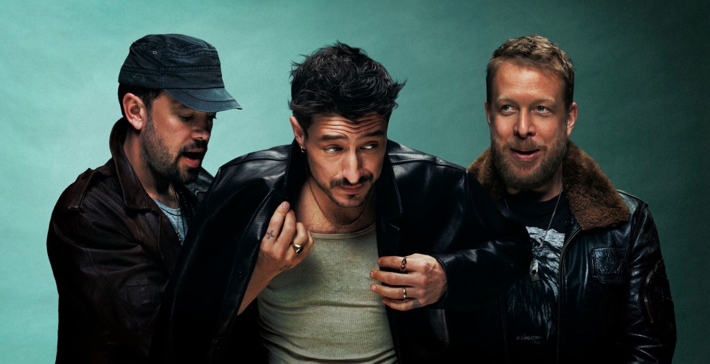 Portrait of English folk rockers Mumford & Sons in front of a teal background.