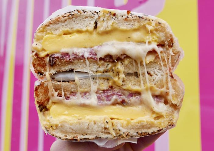 a cheesy bagel sandwich with a pink and yellow background