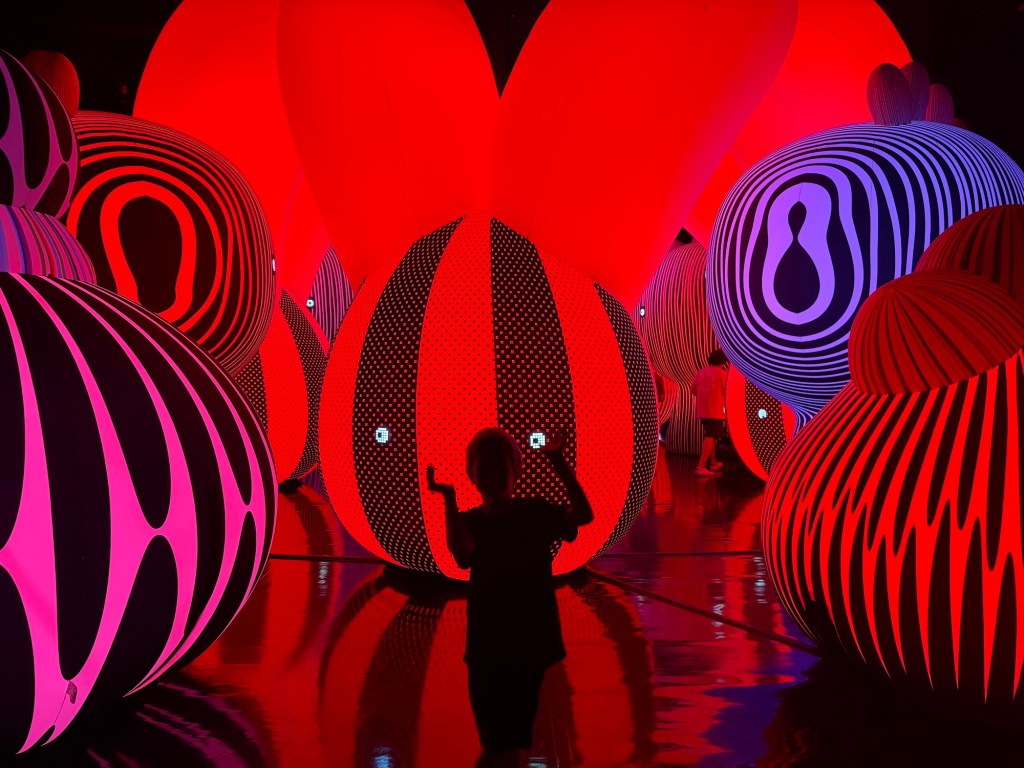 photo of a young child in silhouette in front of giant lit up balloons inside an experiential museum