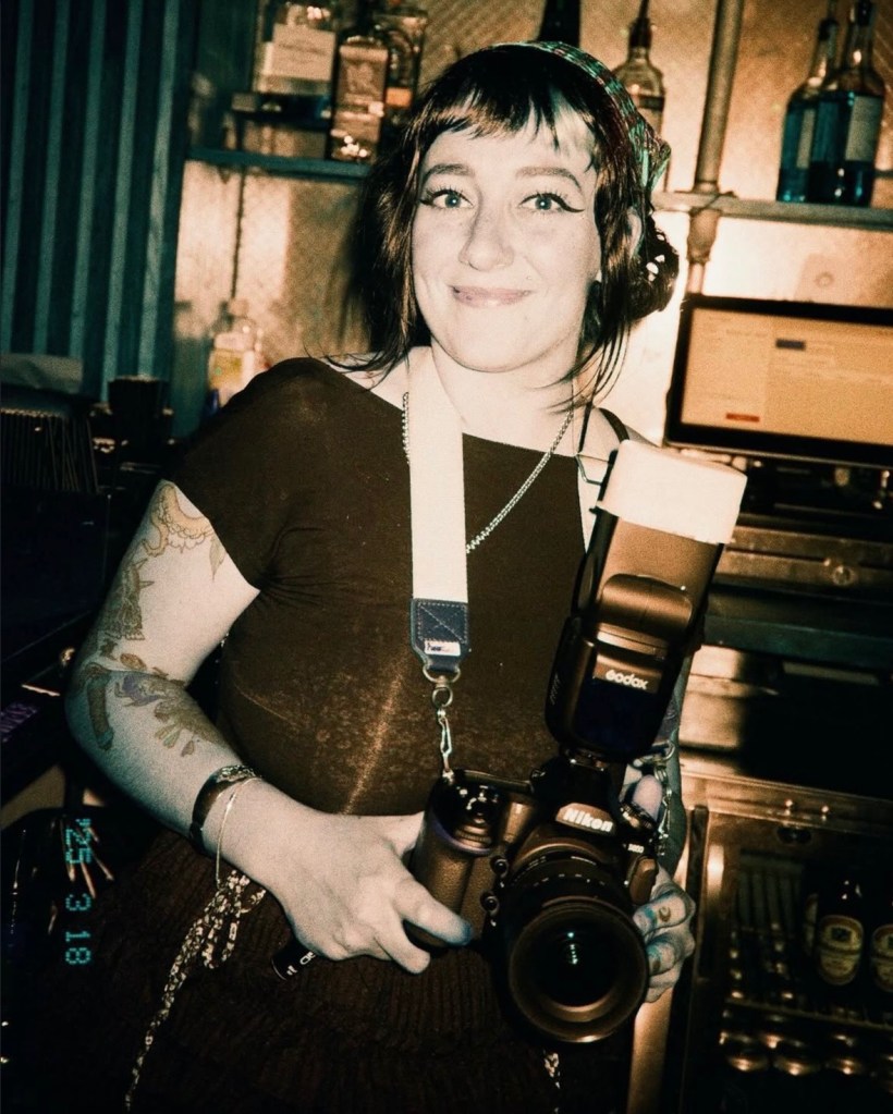 Photo of a young brunette woman holding a camera.