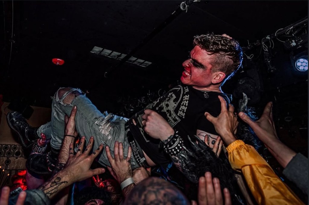 Photo of a man with red pain on his face crowdsurfing during a concert in Miami.