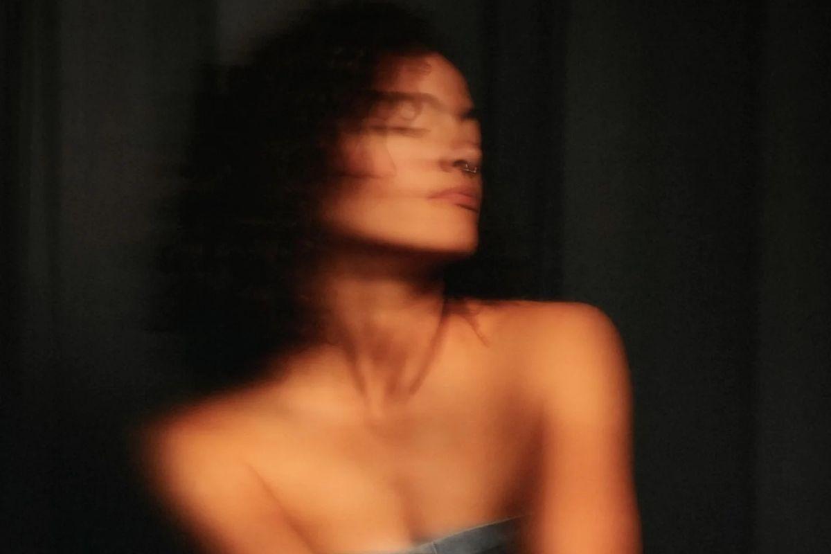 Blurry photo of a woman looking away from the camera wearing a denim strapless top.