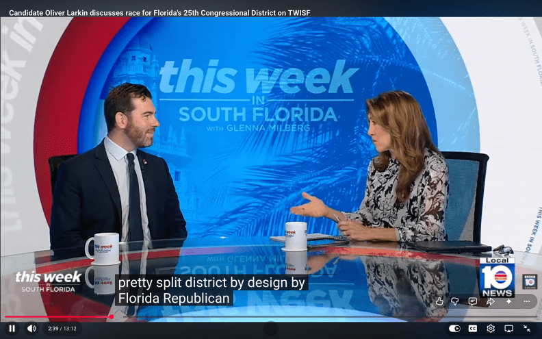 a bearded man talks to a reporter at a TV news desk
