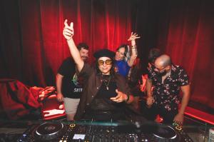 photo of a DJ behind a booth with several friends behind her at a party