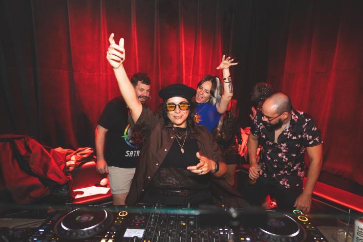 photo of a DJ behind a booth with several friends behind her at a party