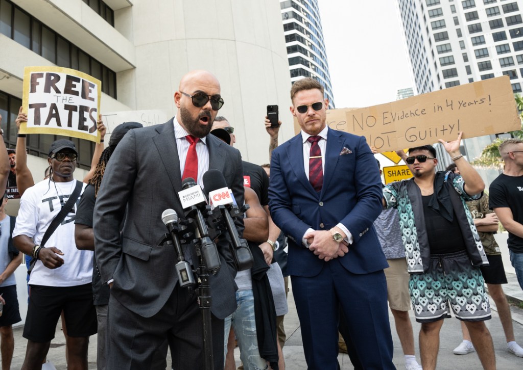 two suited men stand in front of protestors.