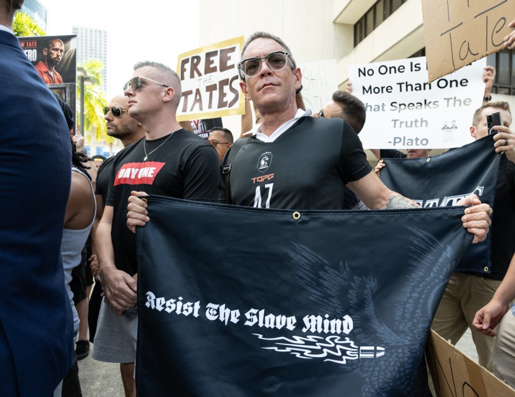a man holds a sign that reads "resist the slave mind."