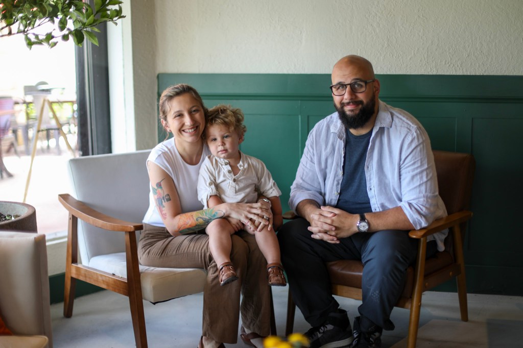 a couple and their child posing for a photo in front of a green wall