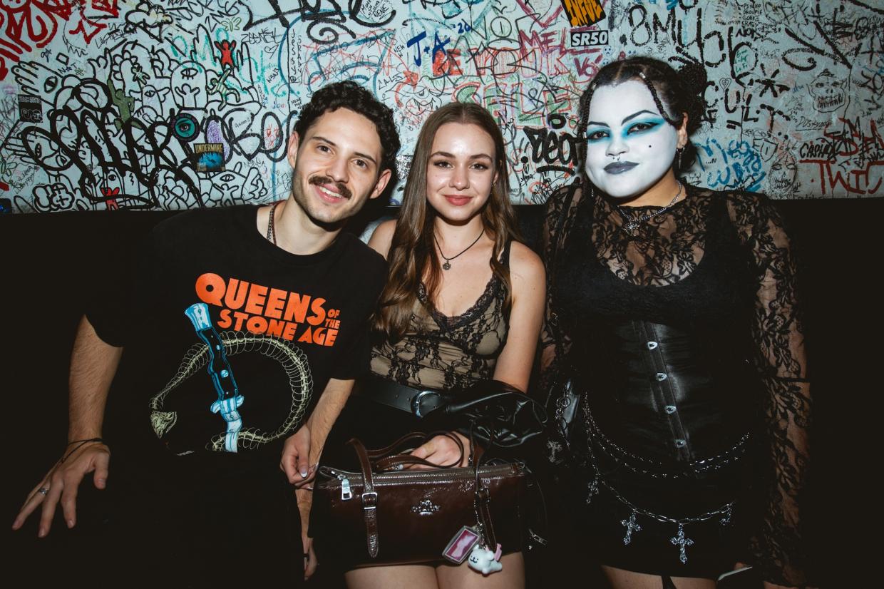 Photo of three people posing for the camera, one is wearing white face paint with light blue eye shadow