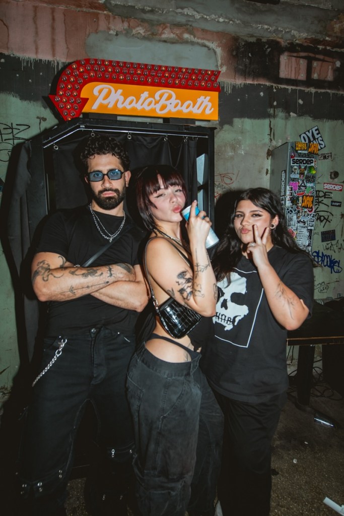 Photo of three people wearing black posing for the camera in front of a photo booth