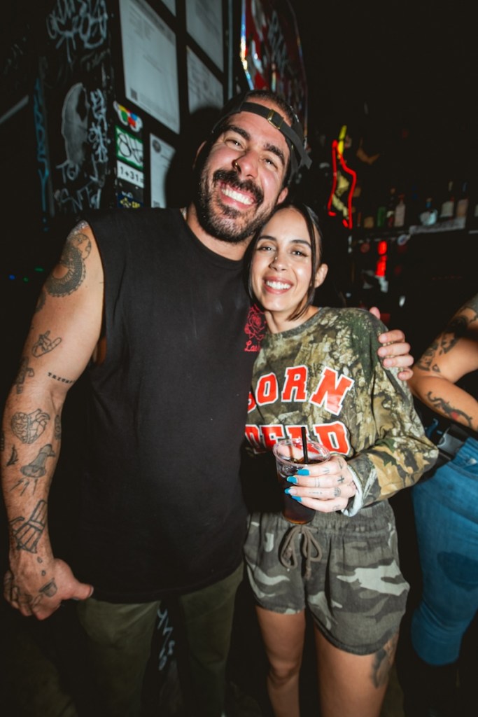 Photo of a tattooed man and a brunette woman smiling and posing for the camera
