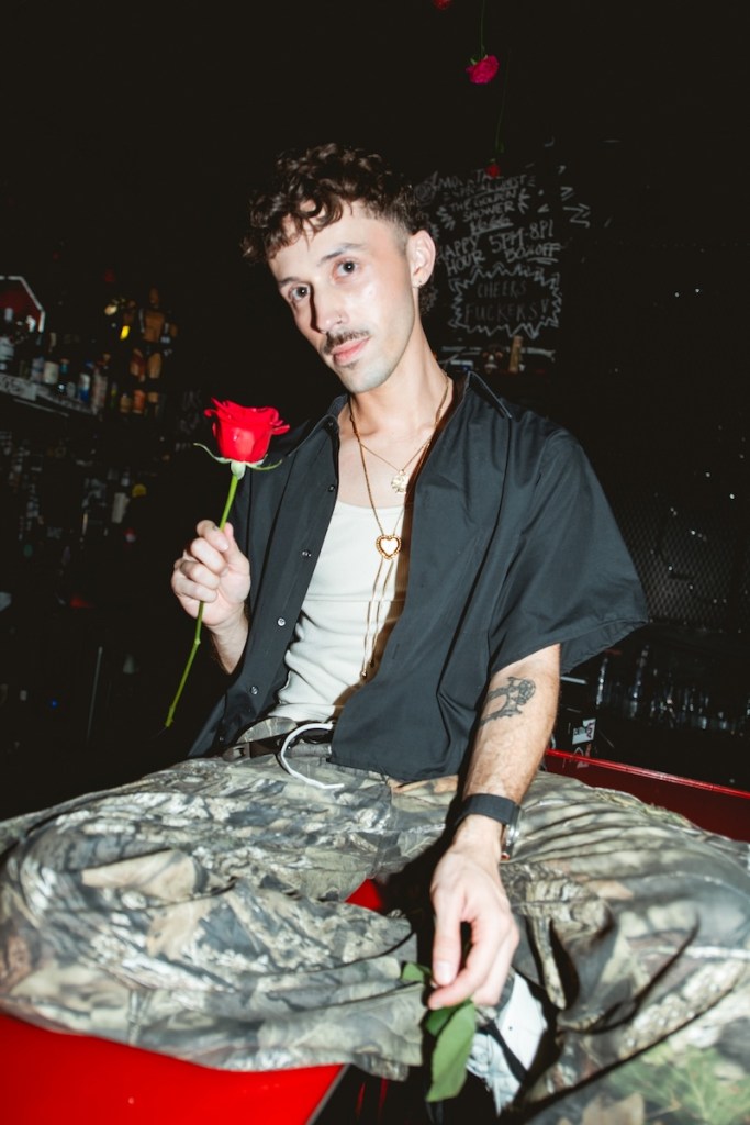 Photo of a young man sitting at the bar holding a red rose