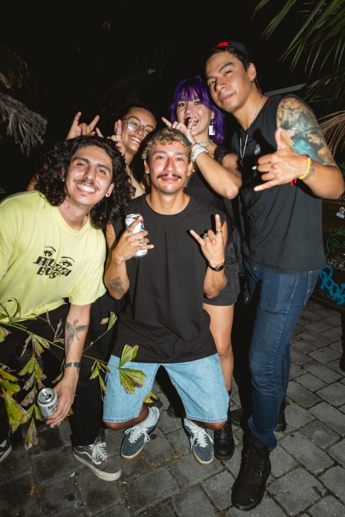 Photo of a group of five people with tattos and holding beer cans posing for the camera
