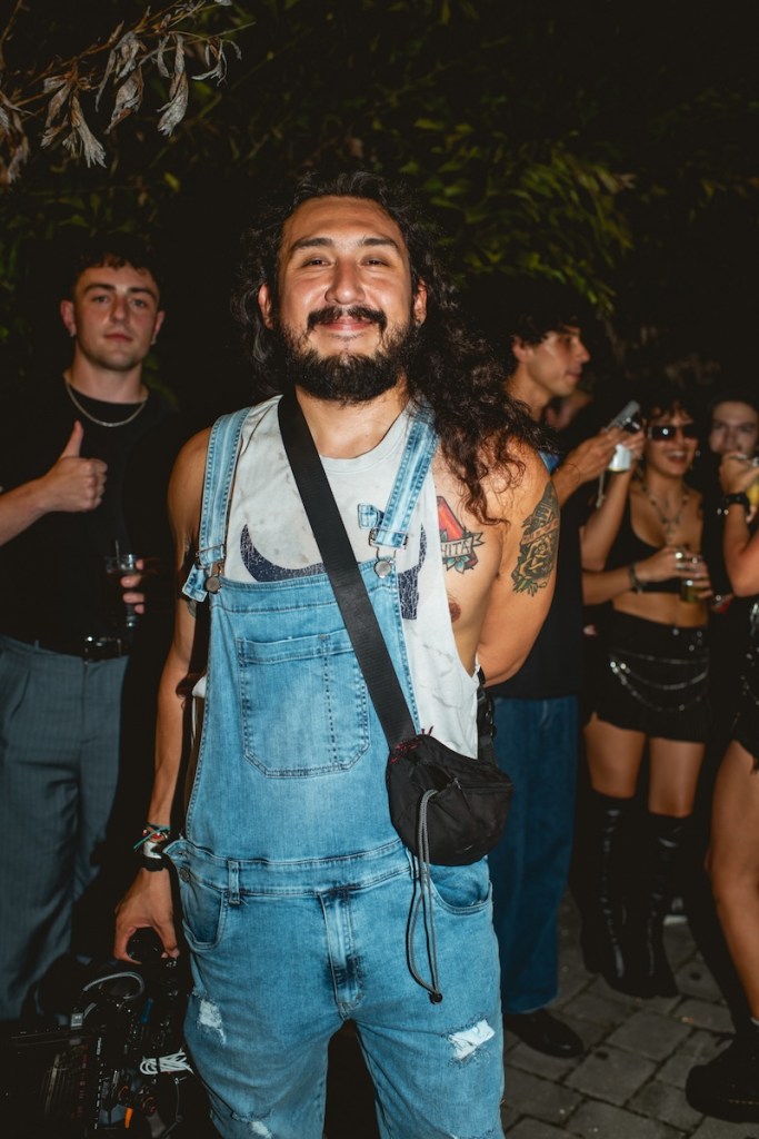 Photo of a man wearing a denim onesie and holding a video camera