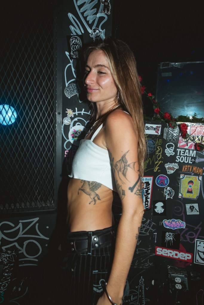 Photo of a blonde woman with long hair wearing a white crop top and black pants