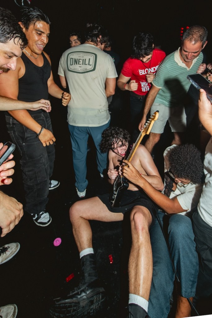 Photo of a guitar player playing guitar on the floor surrounded by fans