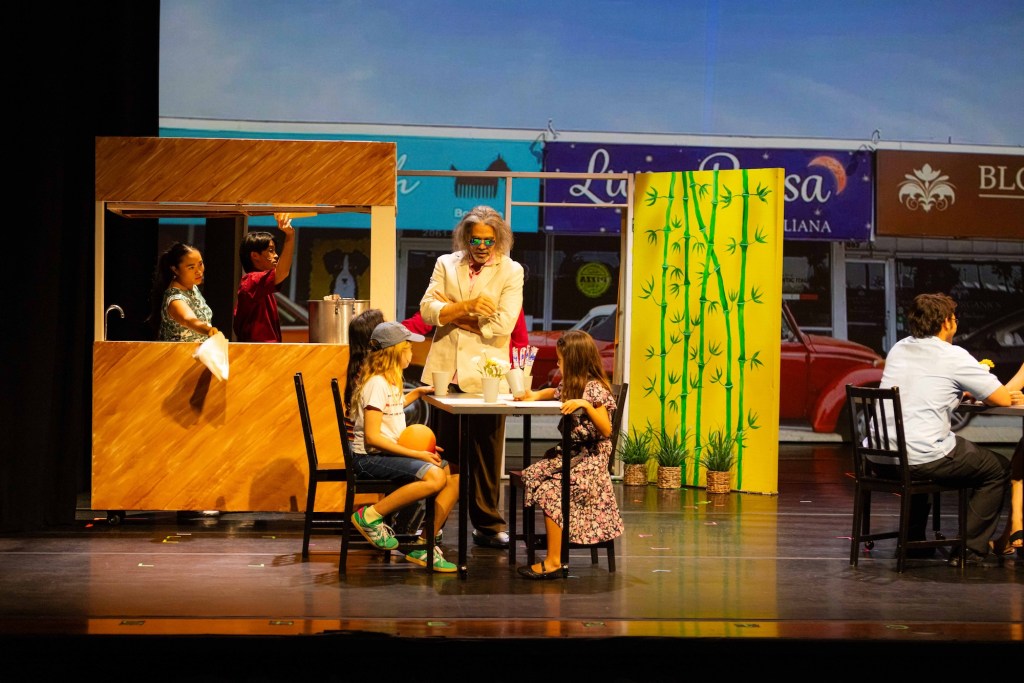 Photo of a stage with actors. The set looks like a restaurant.