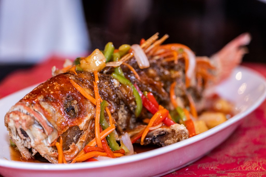 a whole fried fish dish in a white bowl on a red table