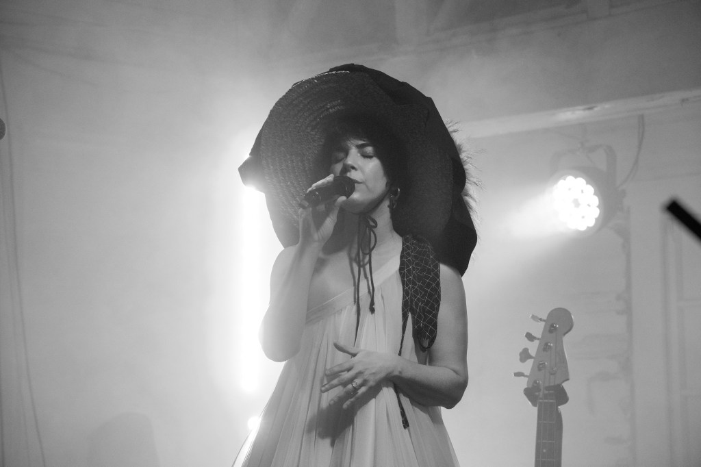 Black and white photo of a woman singing on stage wearing a big black hat