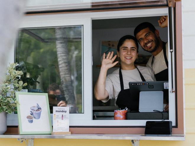 two people wave with glee at a bakery RV window