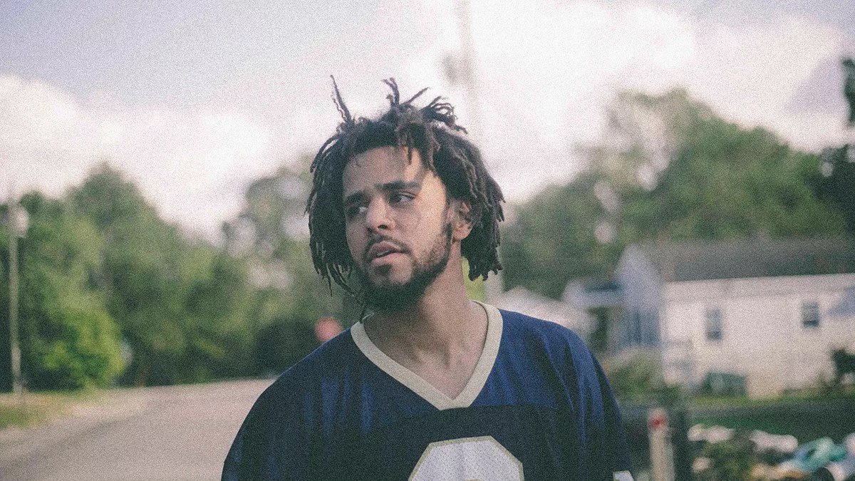 Photo of a man with curly hair outside in a neighborhood with trees