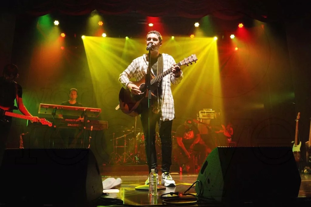 photo of singer Cris Cab performing onstage bathed in yellow, red, and green stage lighting