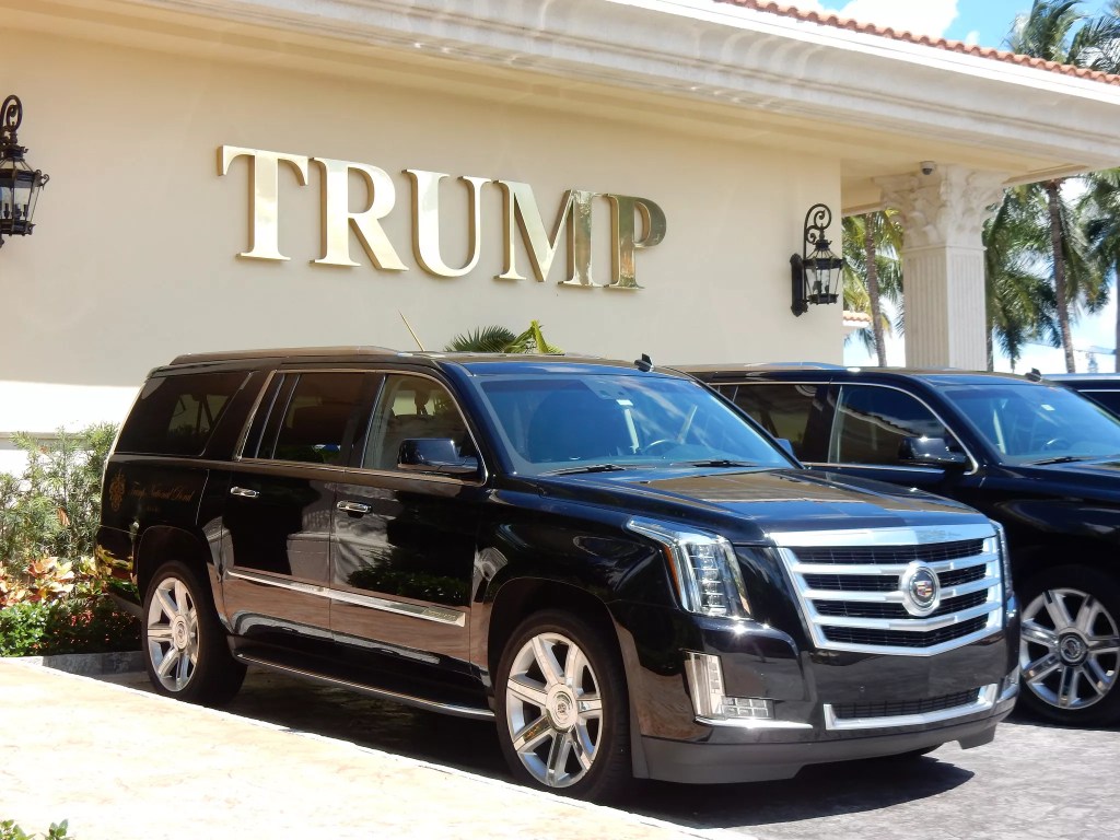 A photo of a Cadillac parked in front of a building with the gold letters "TRUMP" on it. 