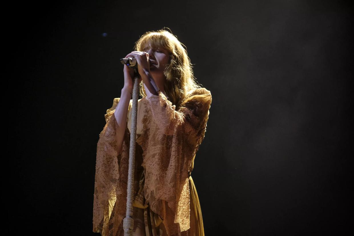 Picture of a woman wearing a yellow dress singing on stage holding a microphone.