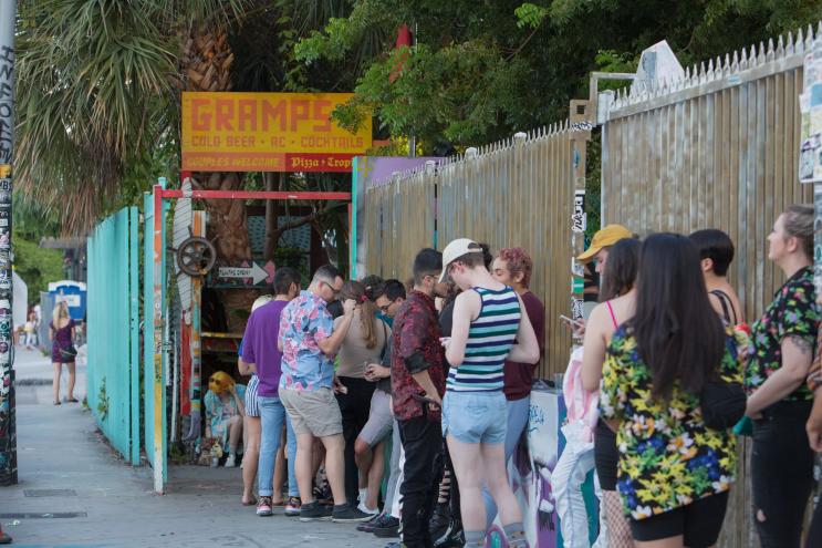 Photo of people in line to enter a bar. A painted wooden sign at the venue reads, "Gramps"