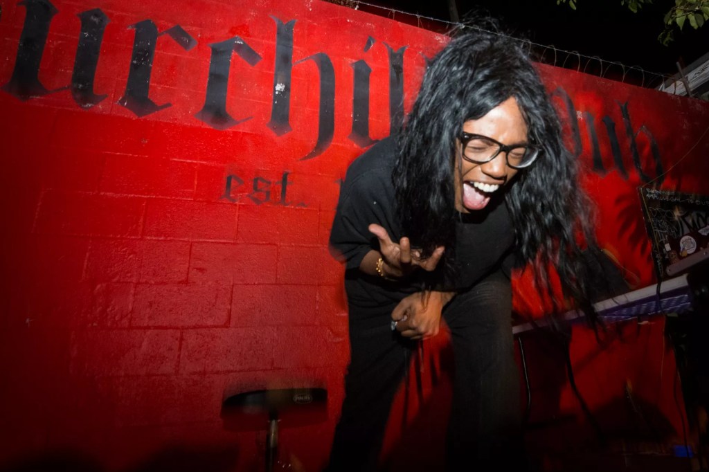 photo of a person screaming on an outdoor stage with a red painted wall behind them