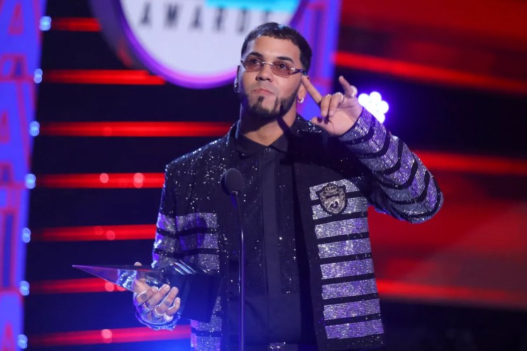 singer Anuel holds a trophy onstage in a bejeweled jacket