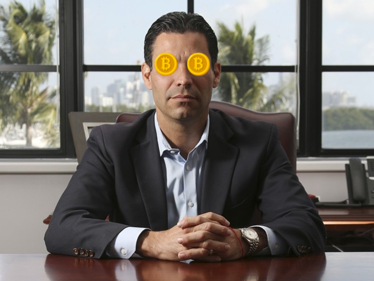 Francis Suarez sits at a desk with his hands folded and two Bitcoin symbols covering his eyes.