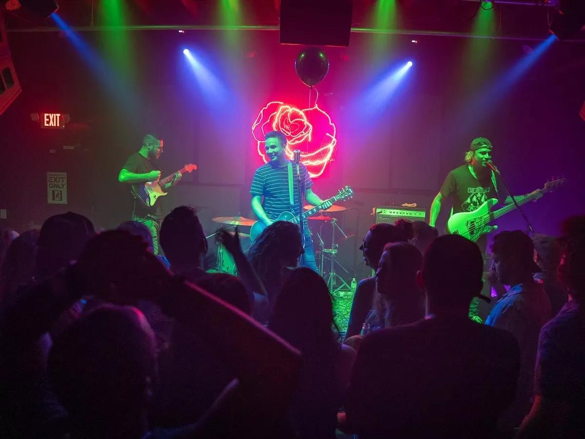 Photo of a stage at Miami venue Las Rosas with a band performing in front of a rose shaped neon sign.