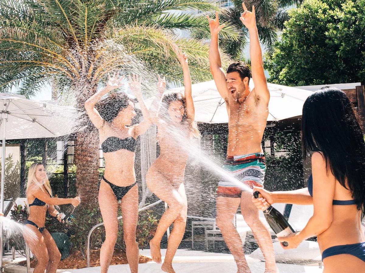 three people dance as someone sprays champagne on them