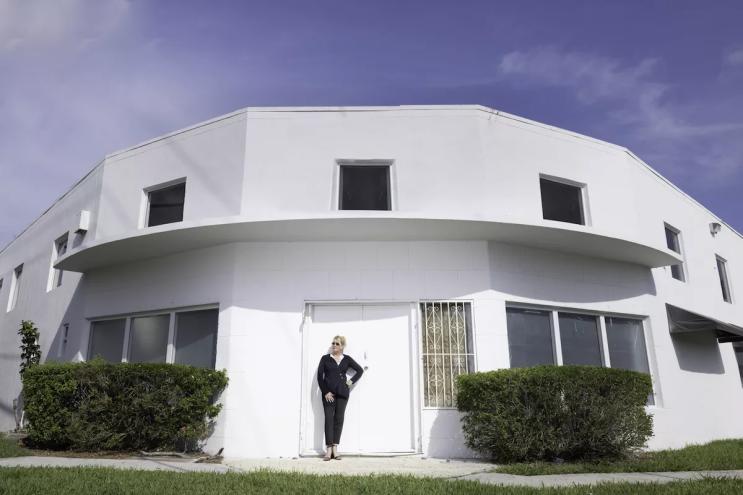 photo of woman standing in the doorway of a two-story white building on a corner lot